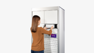 A woman is using a white automated parcel locker to dispatch a package.