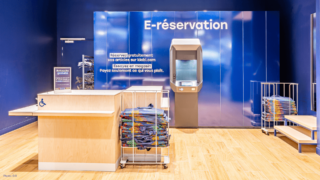 Cleveron 403 robotic parcel locker automating a retail store. The machine is positioned behind a wall, with only the intuitive console visible, providing access for package deposits and retrievals.